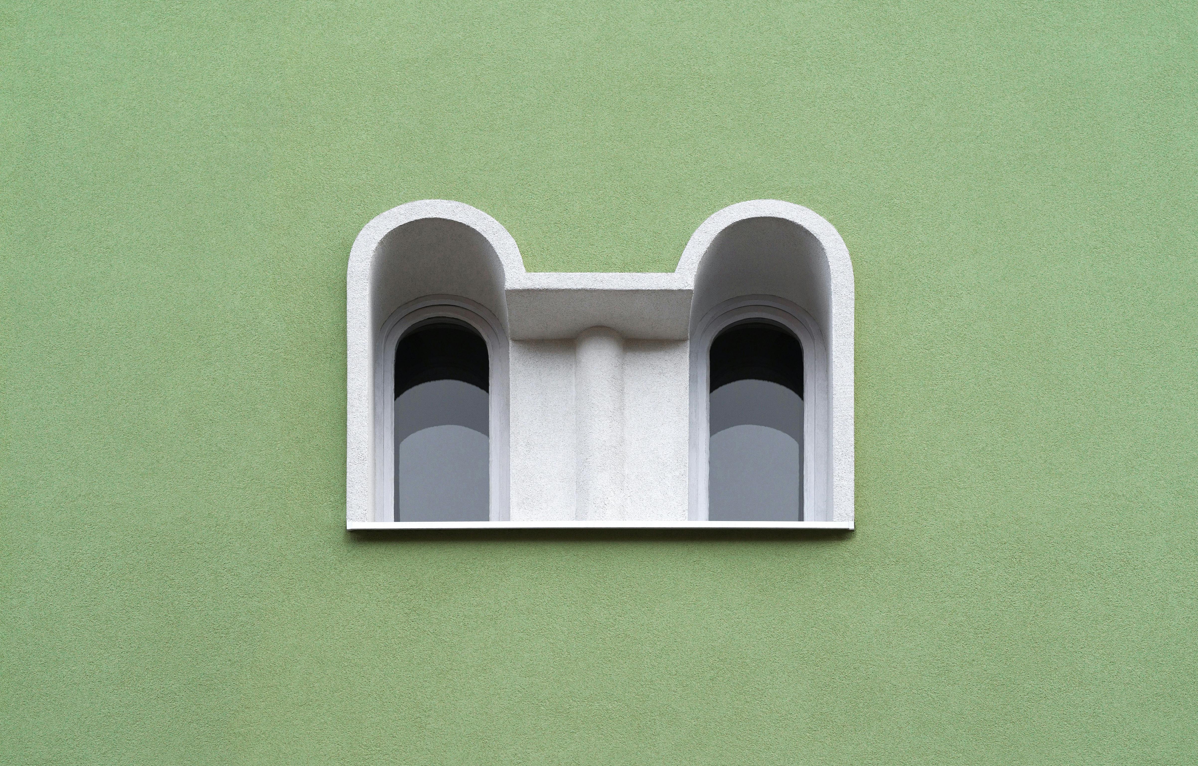 Minimalist architectural design featuring double arched windows against a green wall on a building exterior.