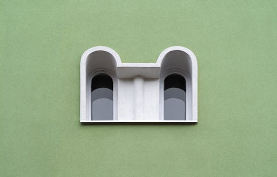 Minimalist architectural design featuring double arched windows against a green wall on a building exterior.