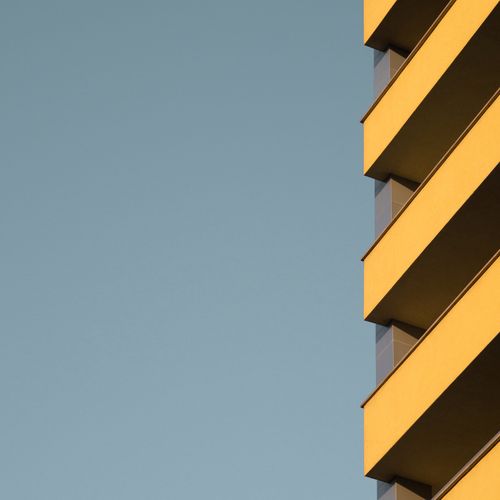 Free A modern yellow building facade contrasts against a clear blue sky, showcasing minimalist architectural design. Stock Photo