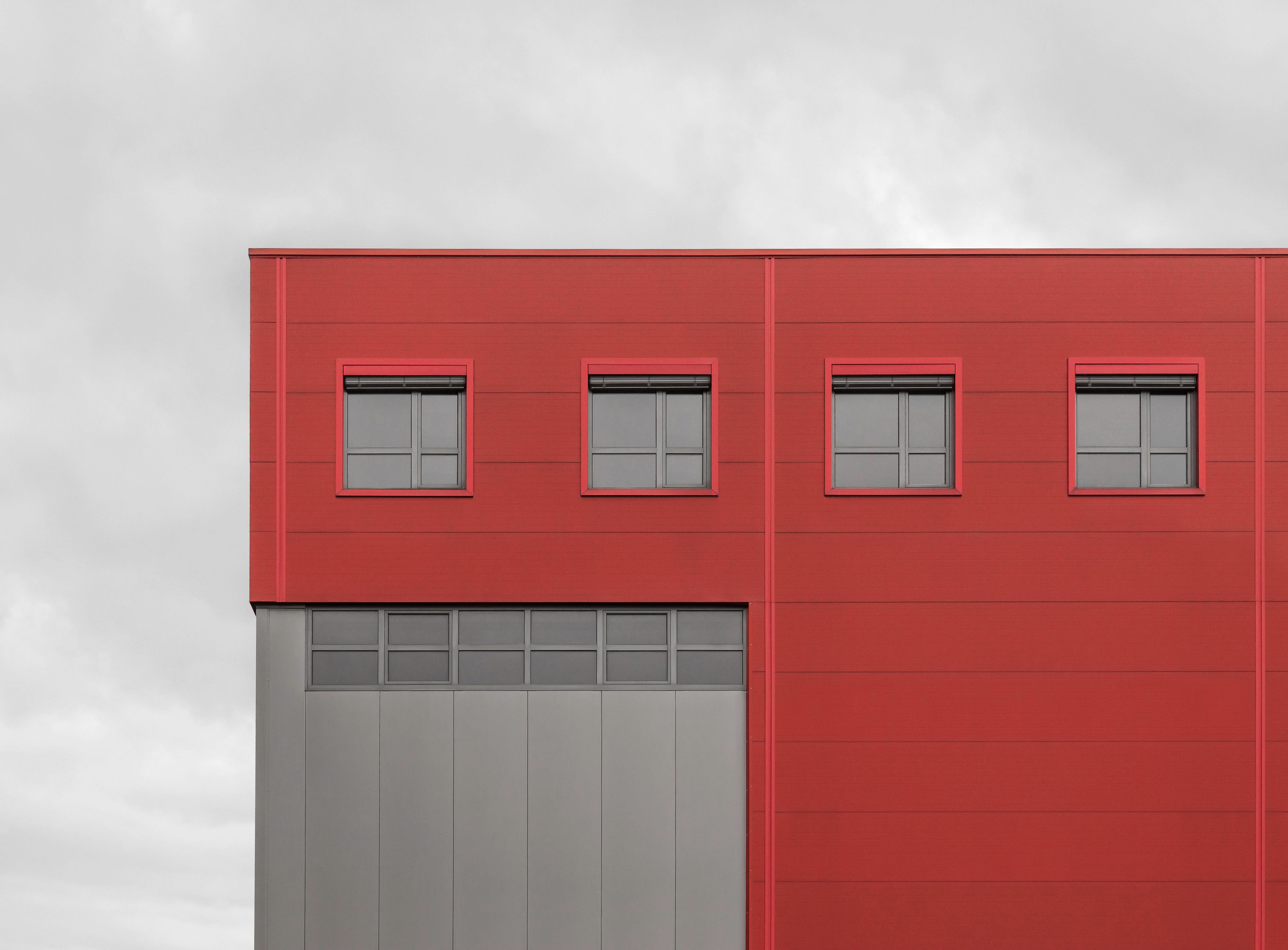 Fotomural Exterior minimalista de un edificio rojo con ventanas negras bajo un cielo nublado.