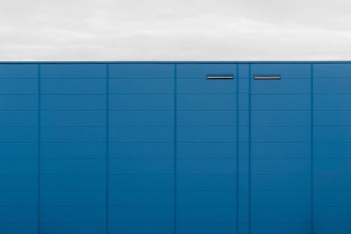 Free A modern blue building facade with clean lines and minimal design against a cloudy sky. Stock Photo