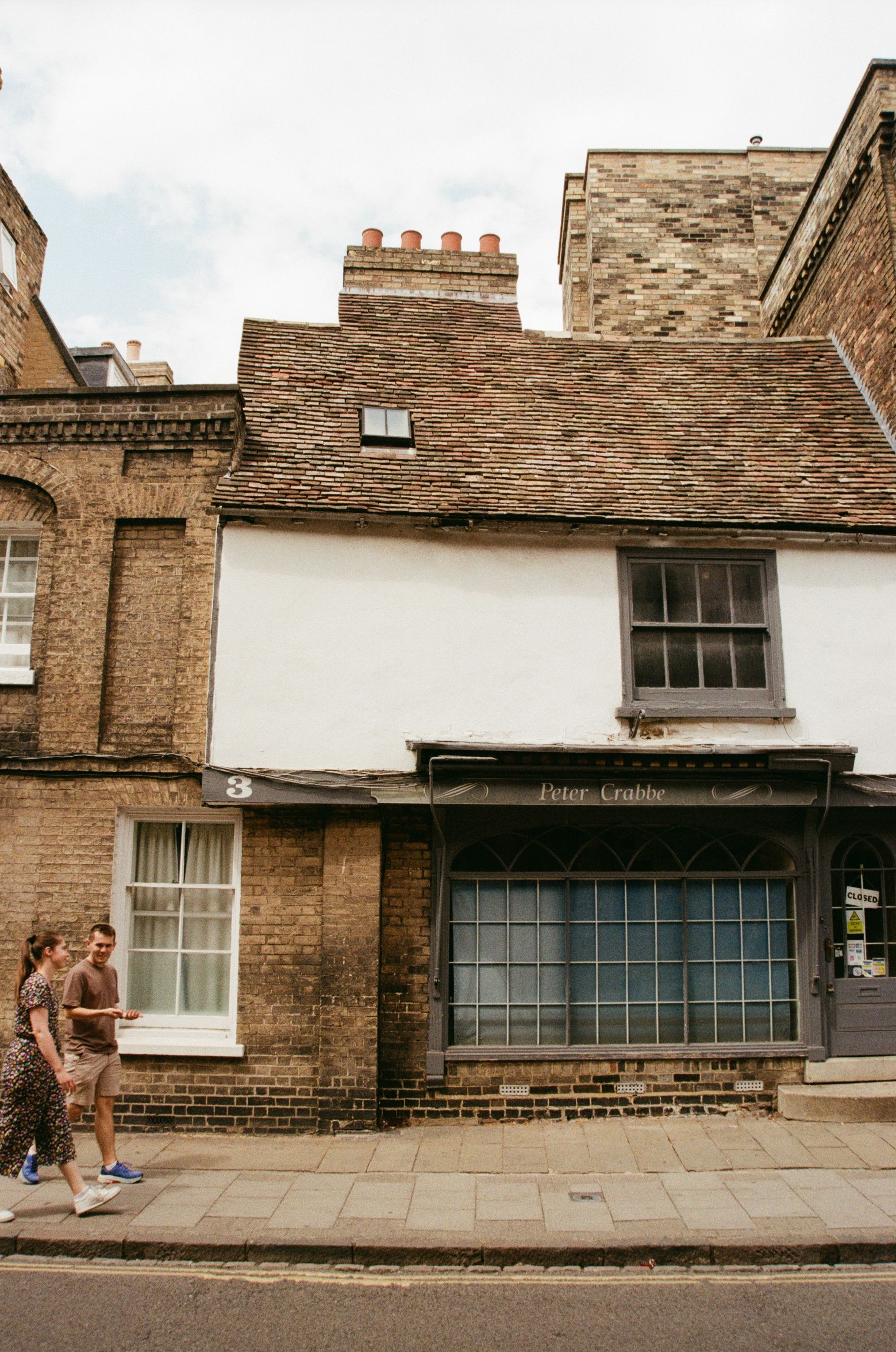 View of a classic brick building in Cambridge, England with pedestrians walking by.