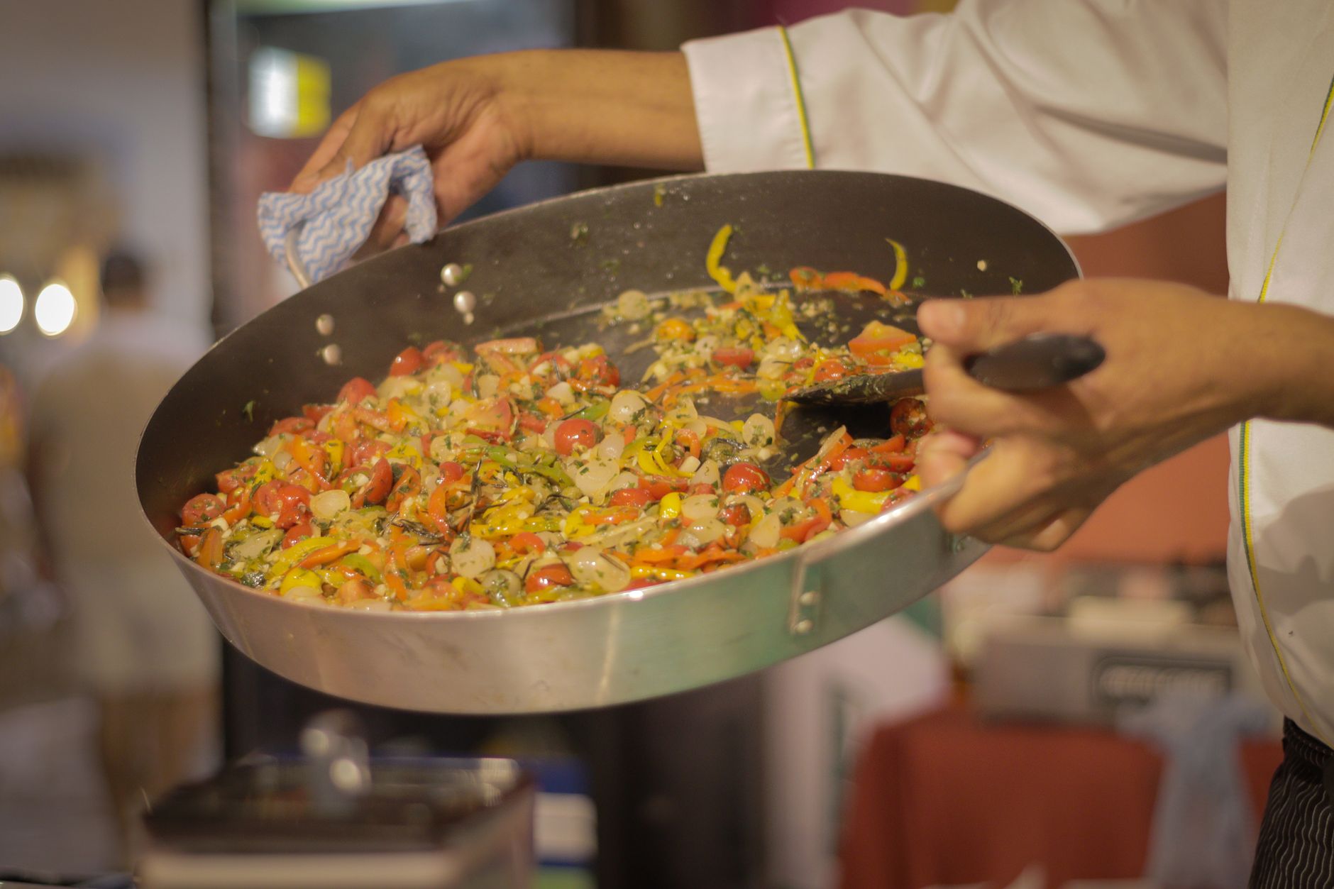A chef preparing a vibrant dish of mixed vegetables in a commercial kitchen setting.