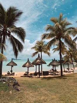 Idyllic tropical beach scene featuring lush palm trees and thatched huts by the sea.