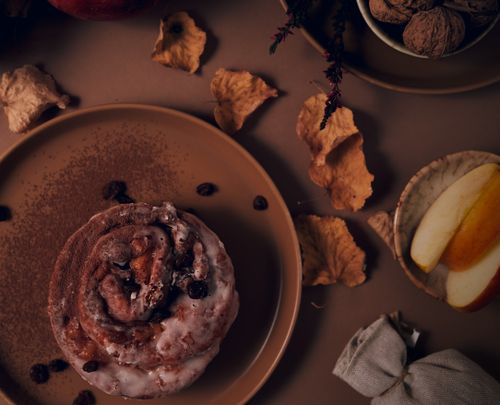 Free Rustic cinnamon roll surrounded by autumn leaves and apples, perfect for fall settings. Stock Photo