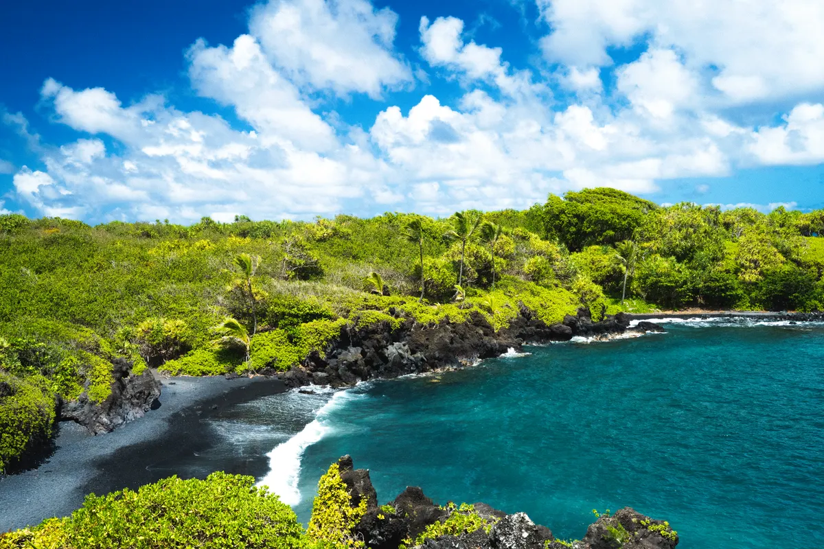 A black sand beach framed by green cliffs and blue water on Maui