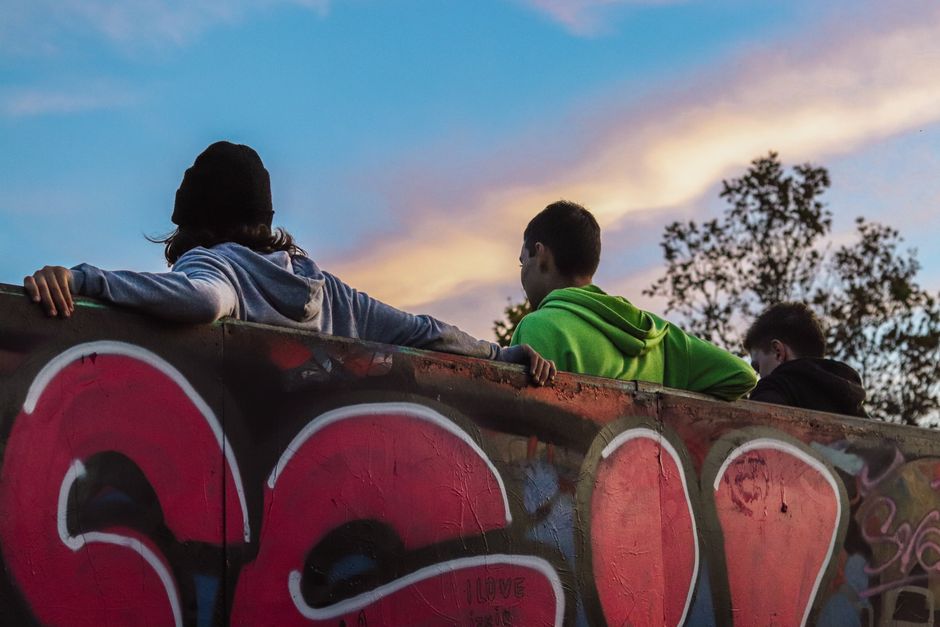 Tres adolescentes se relajan junto a una pared de graffiti al atardecer en un skatepark urbano.