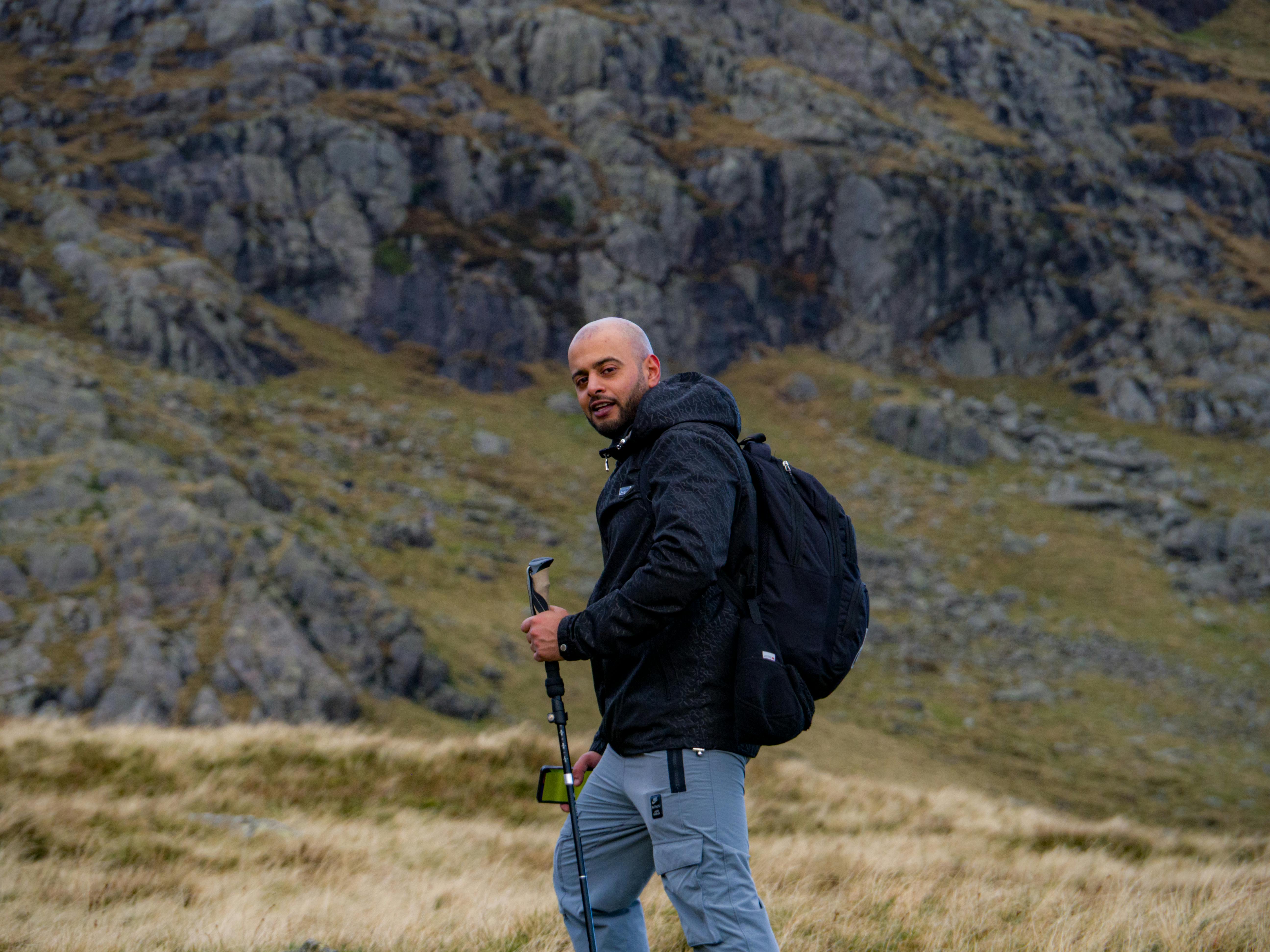 Navigating Permaculture Landscapes - Man hiking with a backpack and trekking pole in rugged, rock
