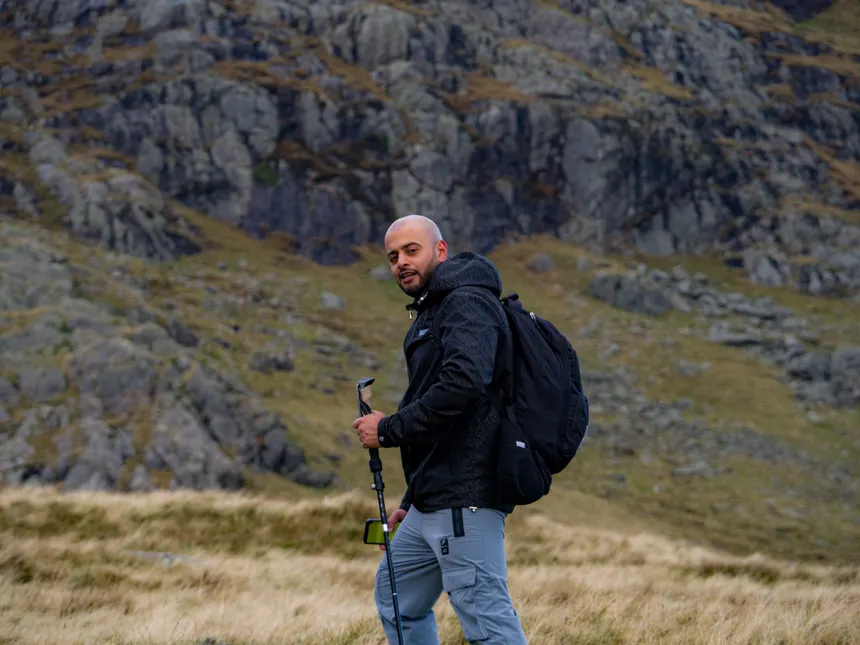 Man hiking with a backpack and trekking pole in rugged, rocky mountain terrain.