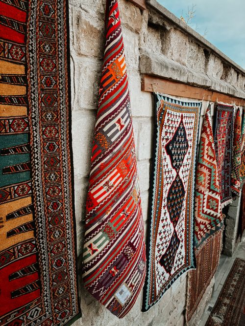 Free Colorful handwoven rugs displayed on a stone wall showcasing intricate traditional patterns. Stock Photo
