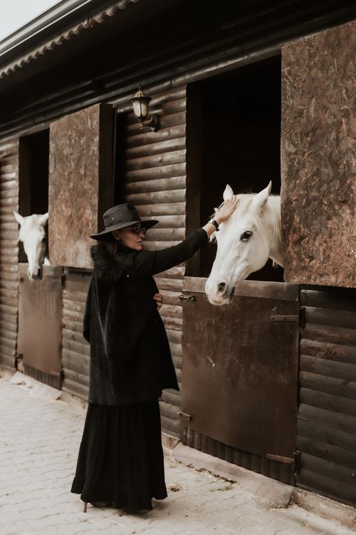 Free Stylish woman in a hat lovingly pets white horses at a stable in Eskişehir, Türkiye. Stock Photo