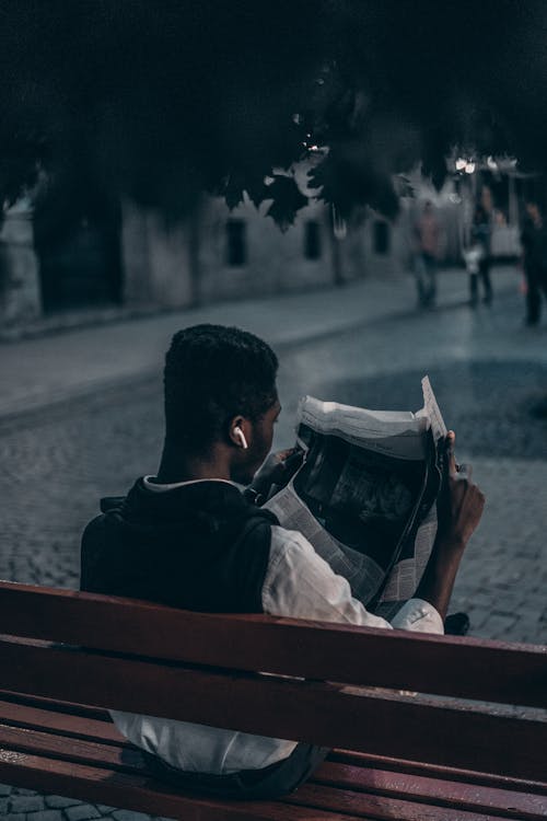 Man Reading a Newspaper Sitting on Wooden Bench