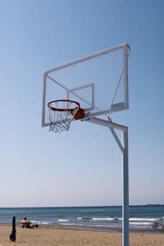 A basketball hoop stands against the backdrop of a serene beach under a clear sky.