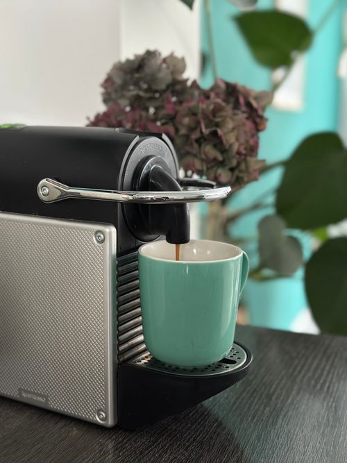 Free Close-up of an espresso machine pouring coffee into a teal mug on a table. Stock Photo