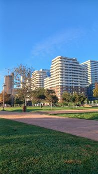 Skyline view of modern high-rise buildings surrounding a green urban park under a clear blue sky.