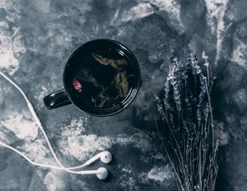 чай в черной керамической кружке возле наушников Apple