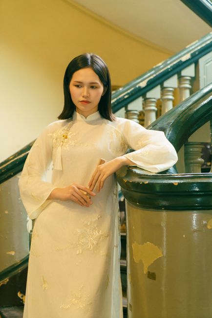 Portrait of a Vietnamese woman in a white ao dai, posing indoors on a spiral staircase.