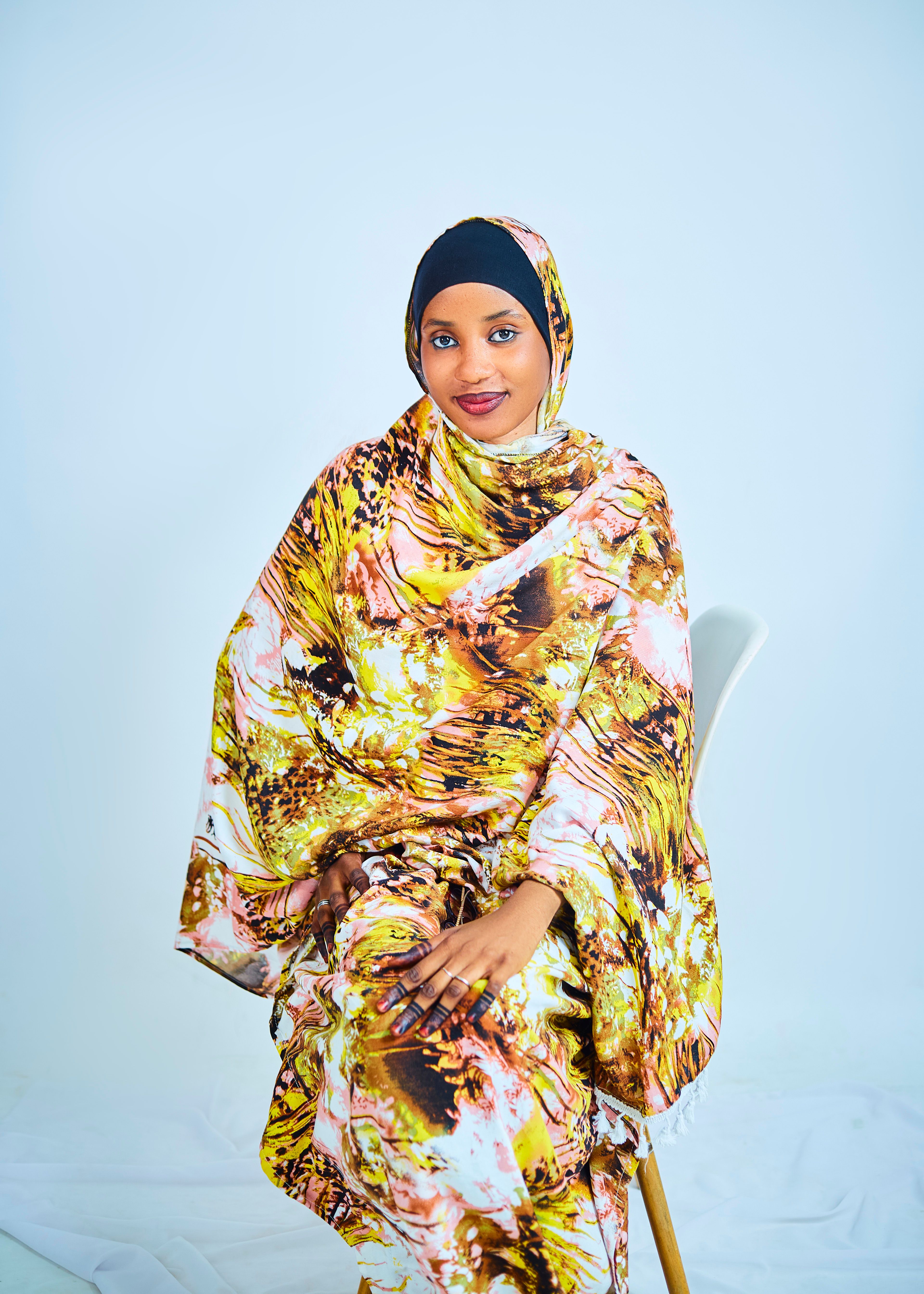 Elegant portrait of an adult woman wearing colorful African dress sitting on a chair indoors.