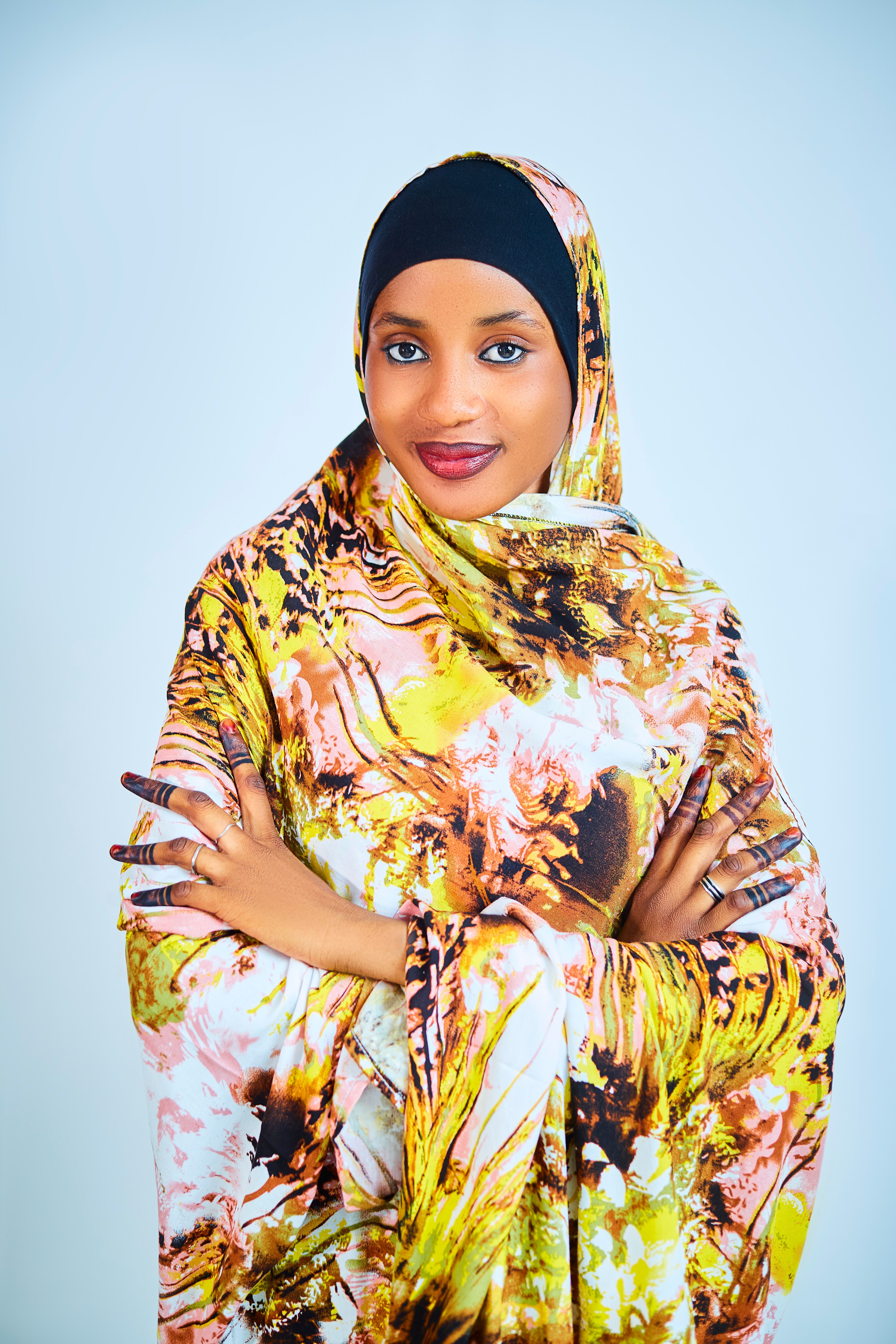 A confident woman wearing a vibrant, floral-patterned hijab smiles warmly.