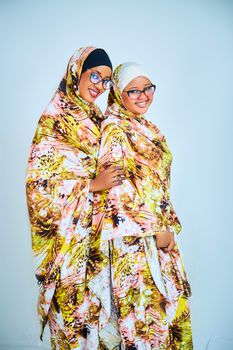 Two women wearing colorful traditional garments, smiling joyfully indoors.