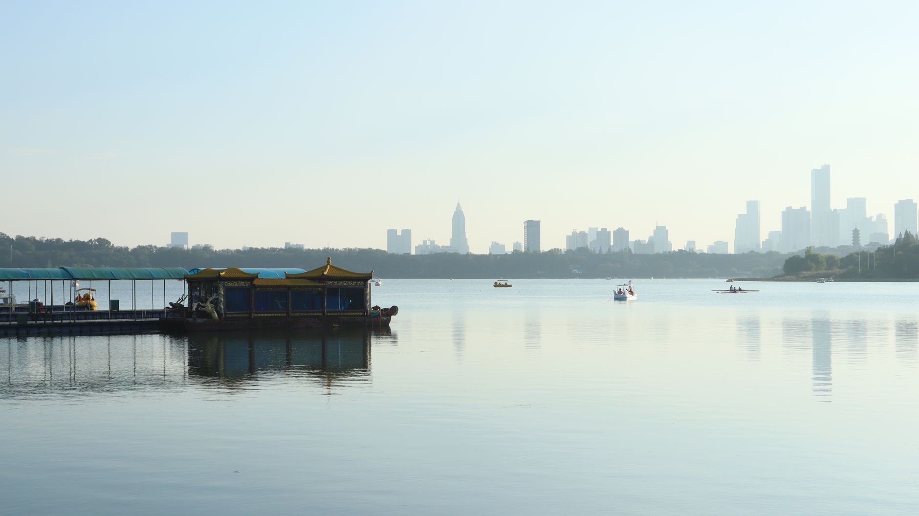Peaceful lakeside view of a city skyline with boats and a floating platform.