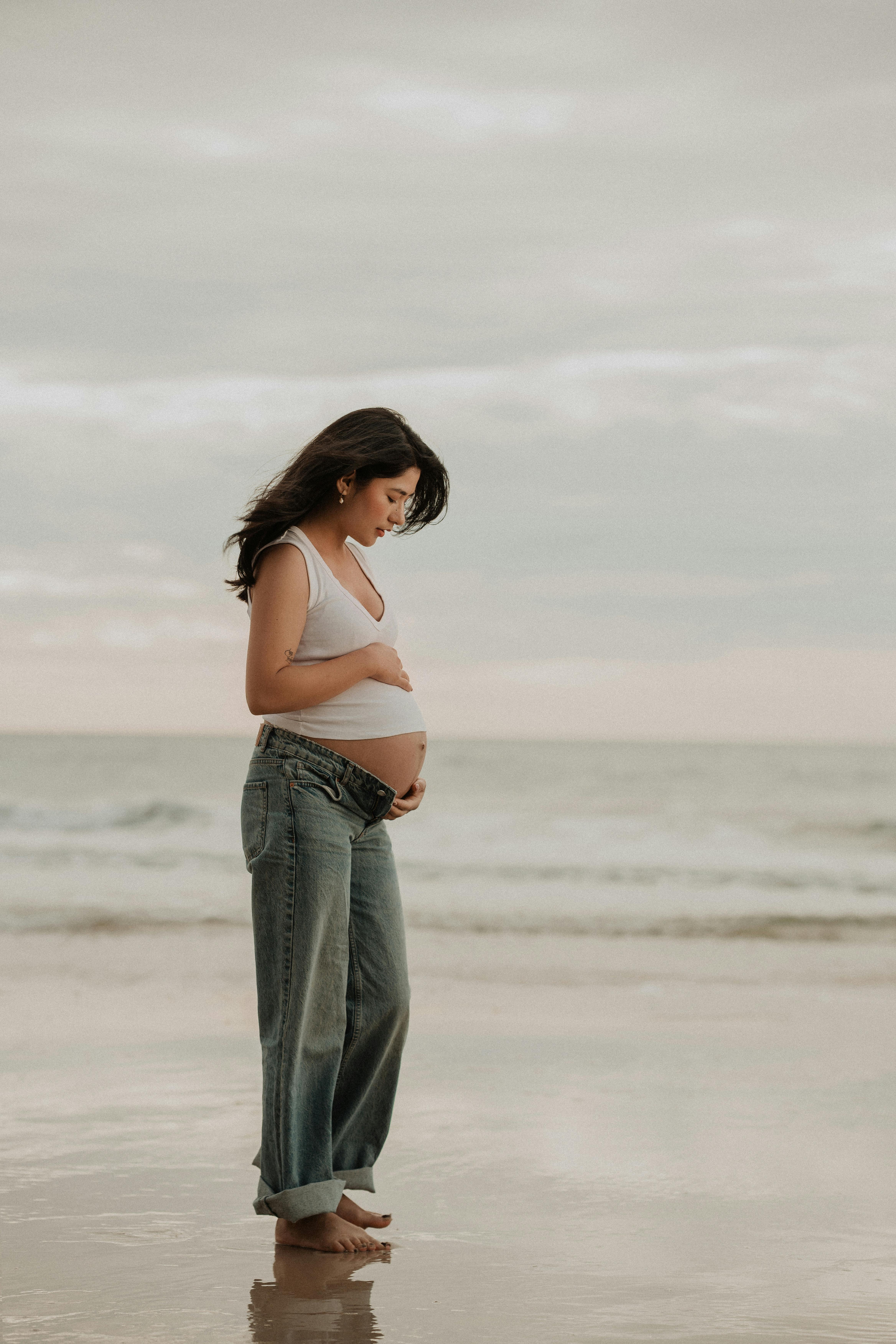 Side view of a pregnant woman standing on a serene beach, embracing tranquility.
