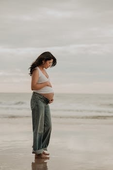 Side view of a pregnant woman standing on a serene beach, embracing tranquility.