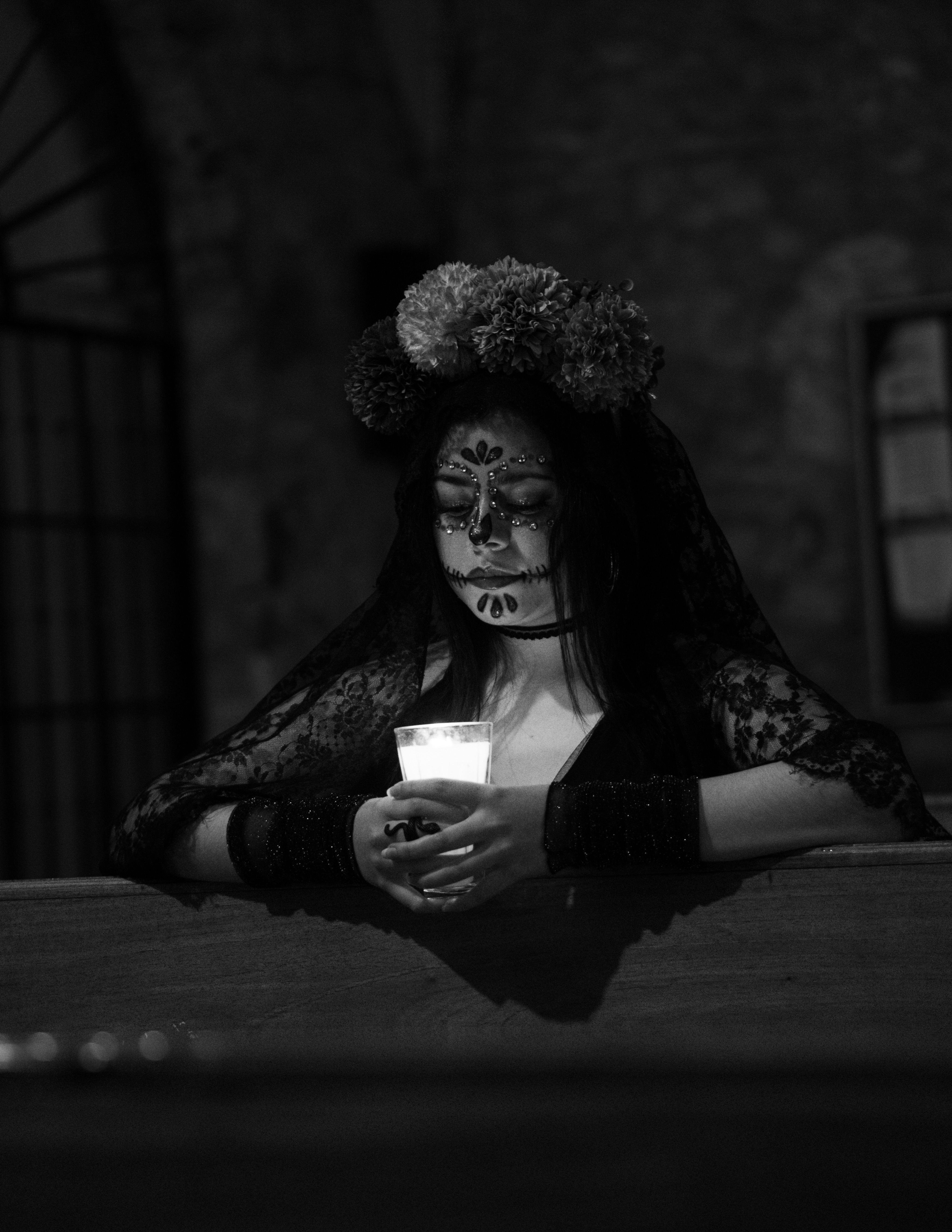 Woman with Day of the Dead makeup holding candle in dark church setting.