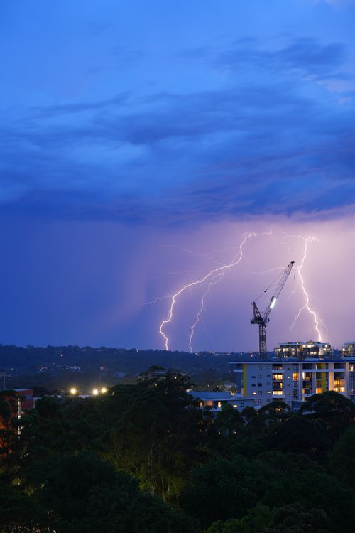 Free Lightning strikes illuminate a cityscape at night with a construction crane silhouette. Stock Photo