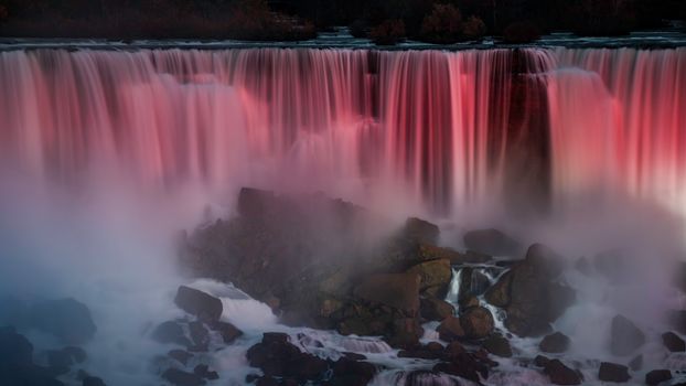 A vibrant long exposure shot of a waterfall illuminated with colorful lights at evening.