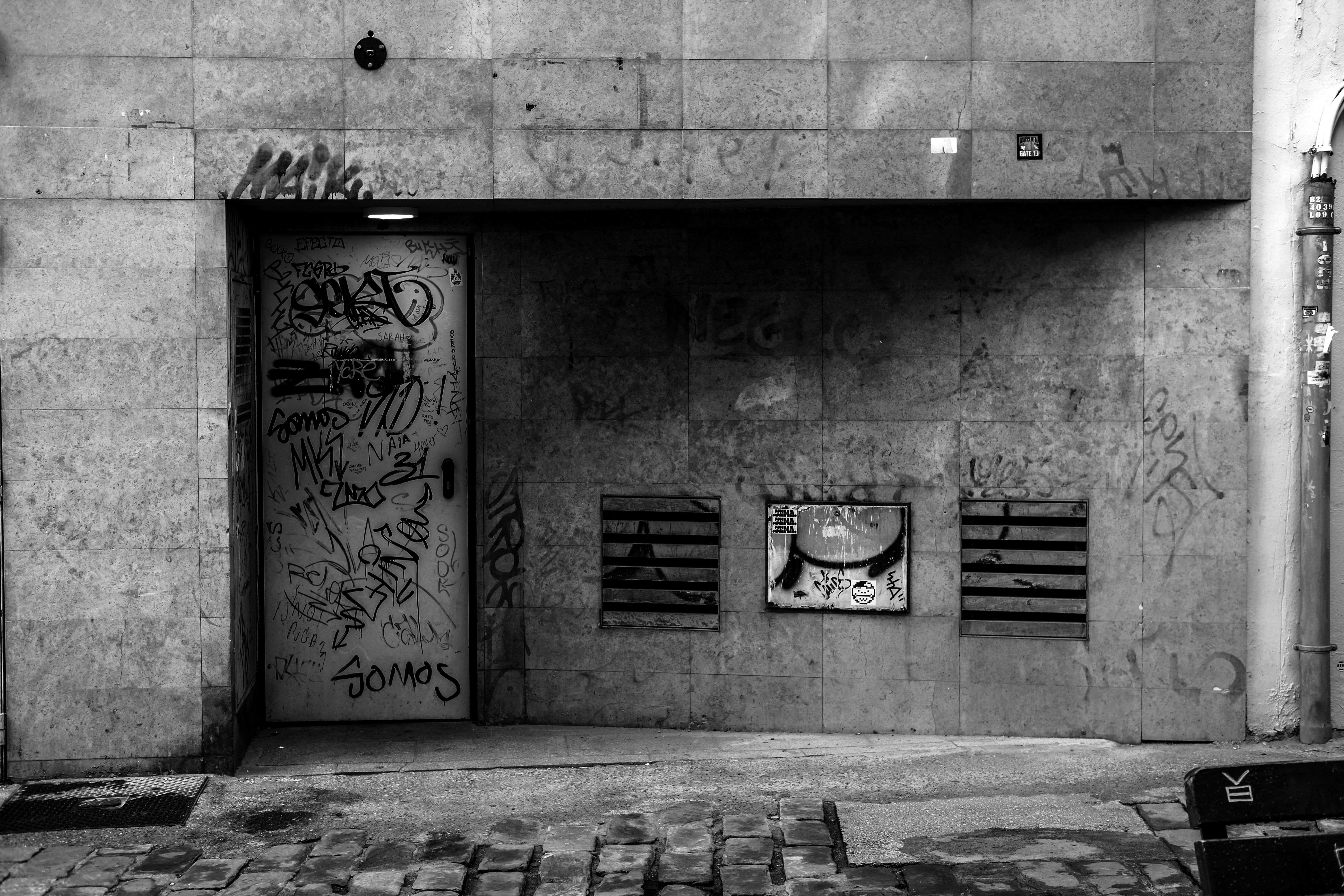 Black and white photograph of a graffiti-covered urban wall in a city setting.