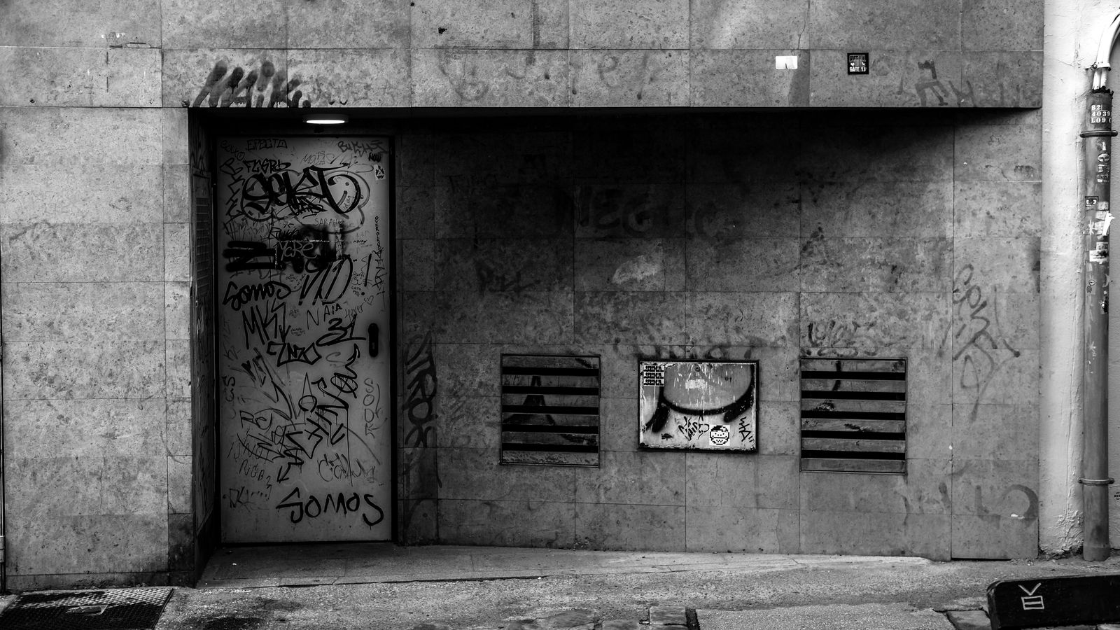 Mur urbain entièrement recouvert de graffitis, photographié en noir et blanc.