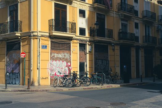 City street corner with bicycles against a graffiti-covered wall under sunlight.
