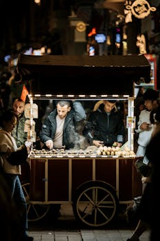Night scene of a street vendor selling roasted chestnuts from a cart in a crowded market.