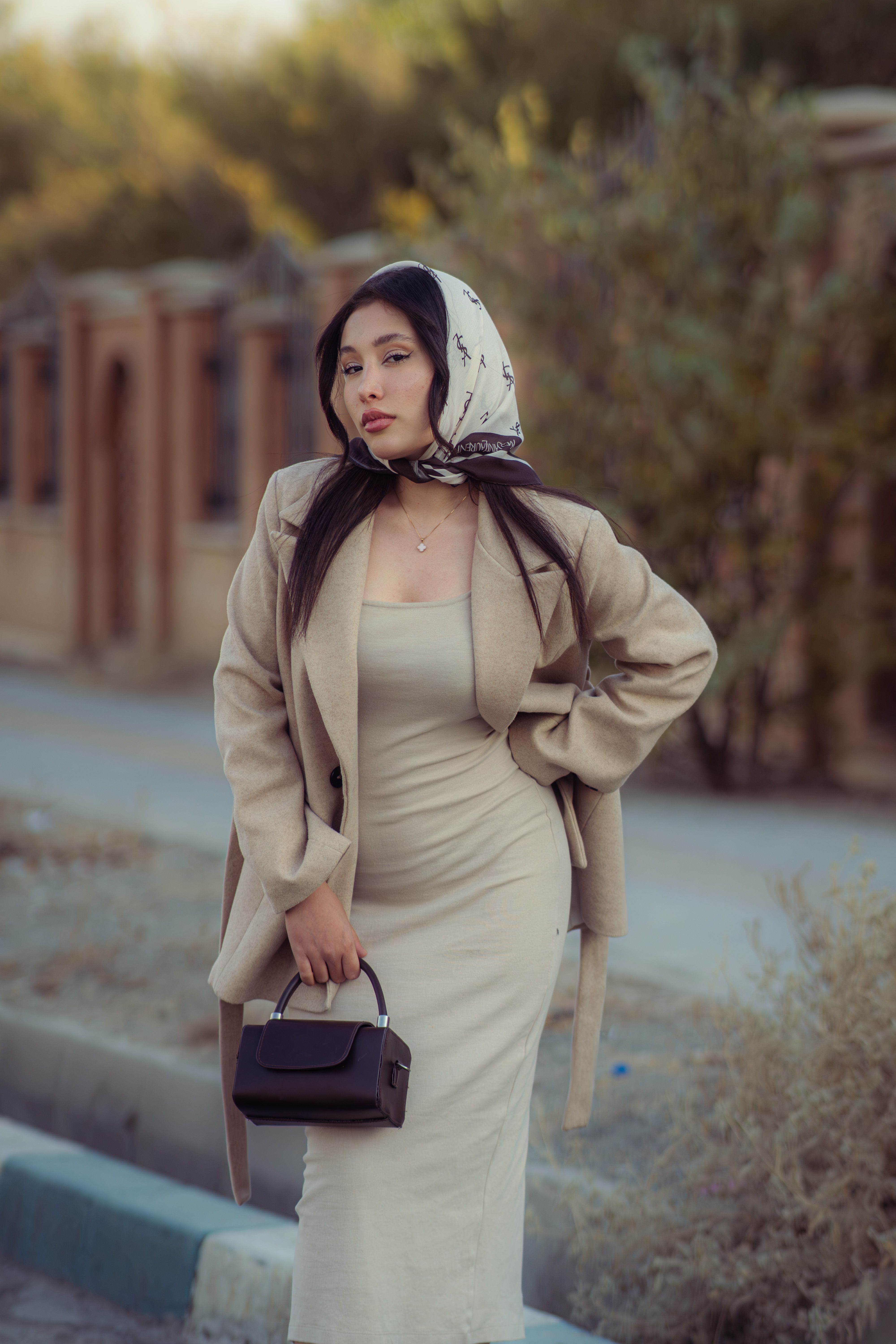 Stylish woman in a beige coat posing outdoors in Tehran, Iran during fall. Fashion and lifestyle portrait.