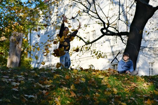 Two children in a Polish park enjoying fall, playing with autumn leaves in daylight.