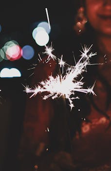 A woman holding a sparkler during Diwali night celebration, blurred festive lights add to the vibrant atmosphere.