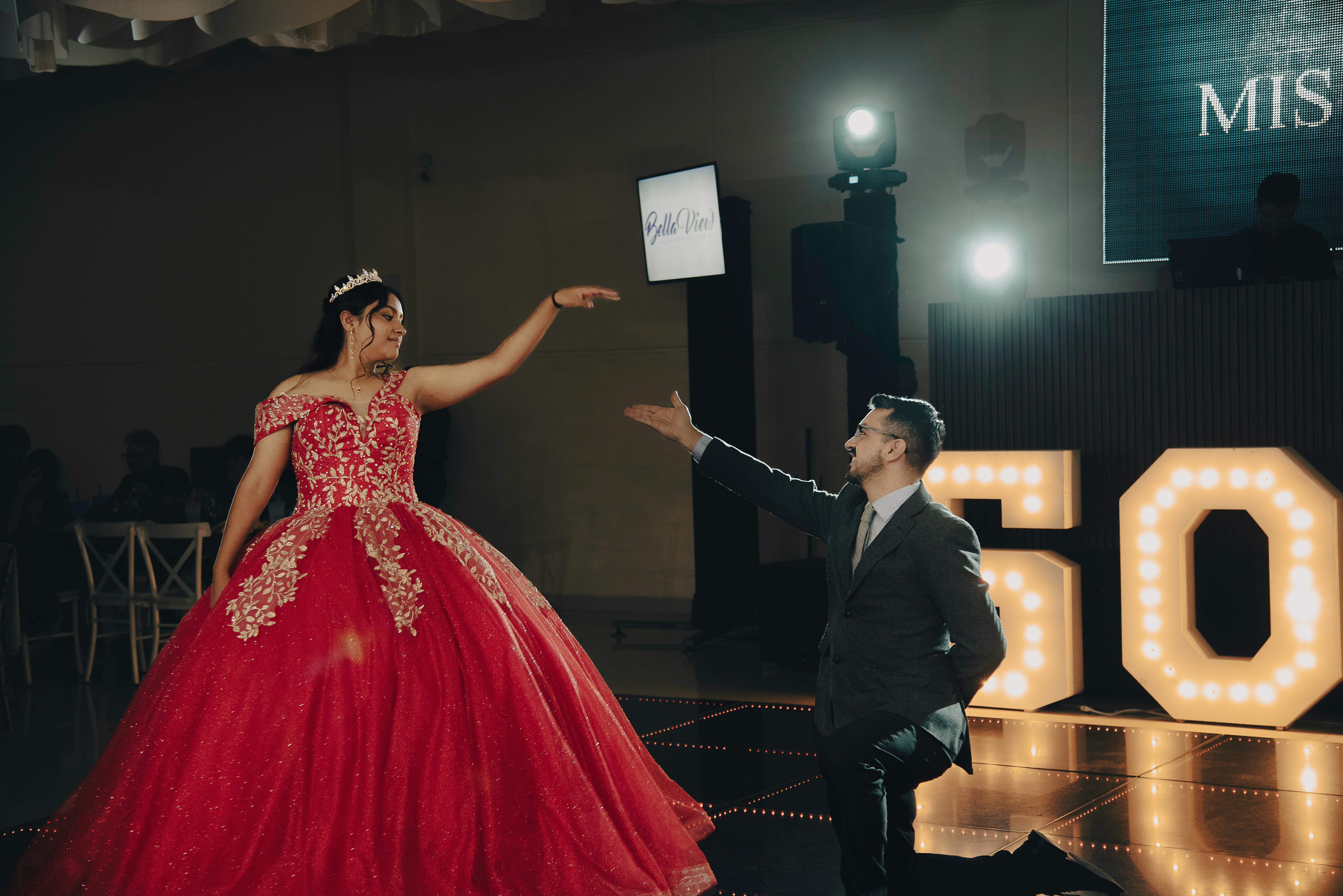 A vibrant quinceañera dance with a young woman in a stunning red gown and tiara, celebrating indoors.