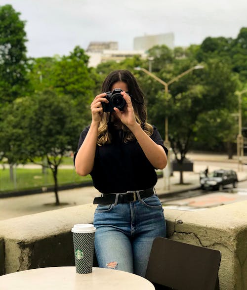 Woman Wearing Black T-shirt and Blue Denim Jeans While Holding Black Dslr Camera