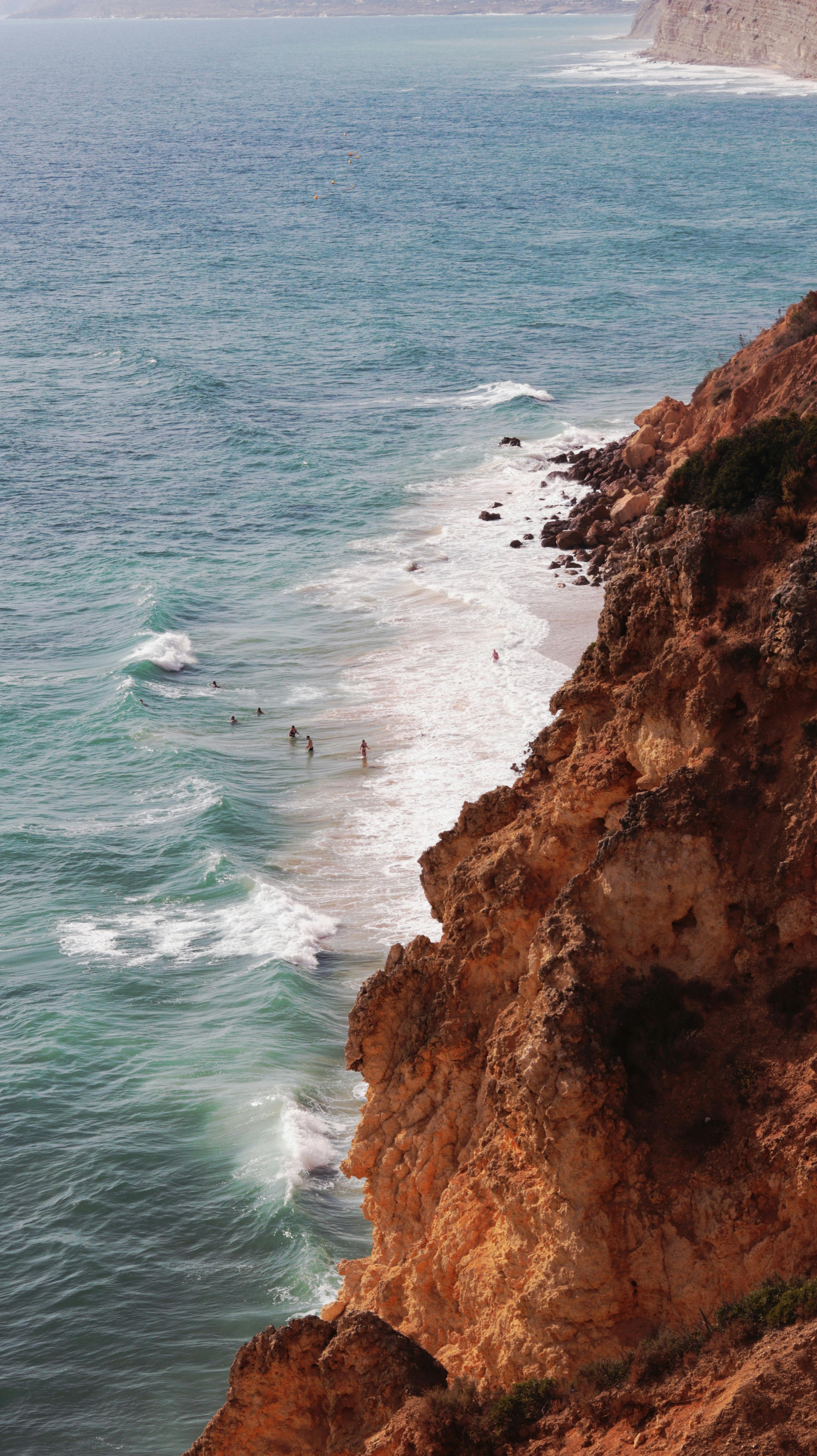 A breathtaking view of rugged cliffs and a serene beach with swimmers enjoying the ocean waves.