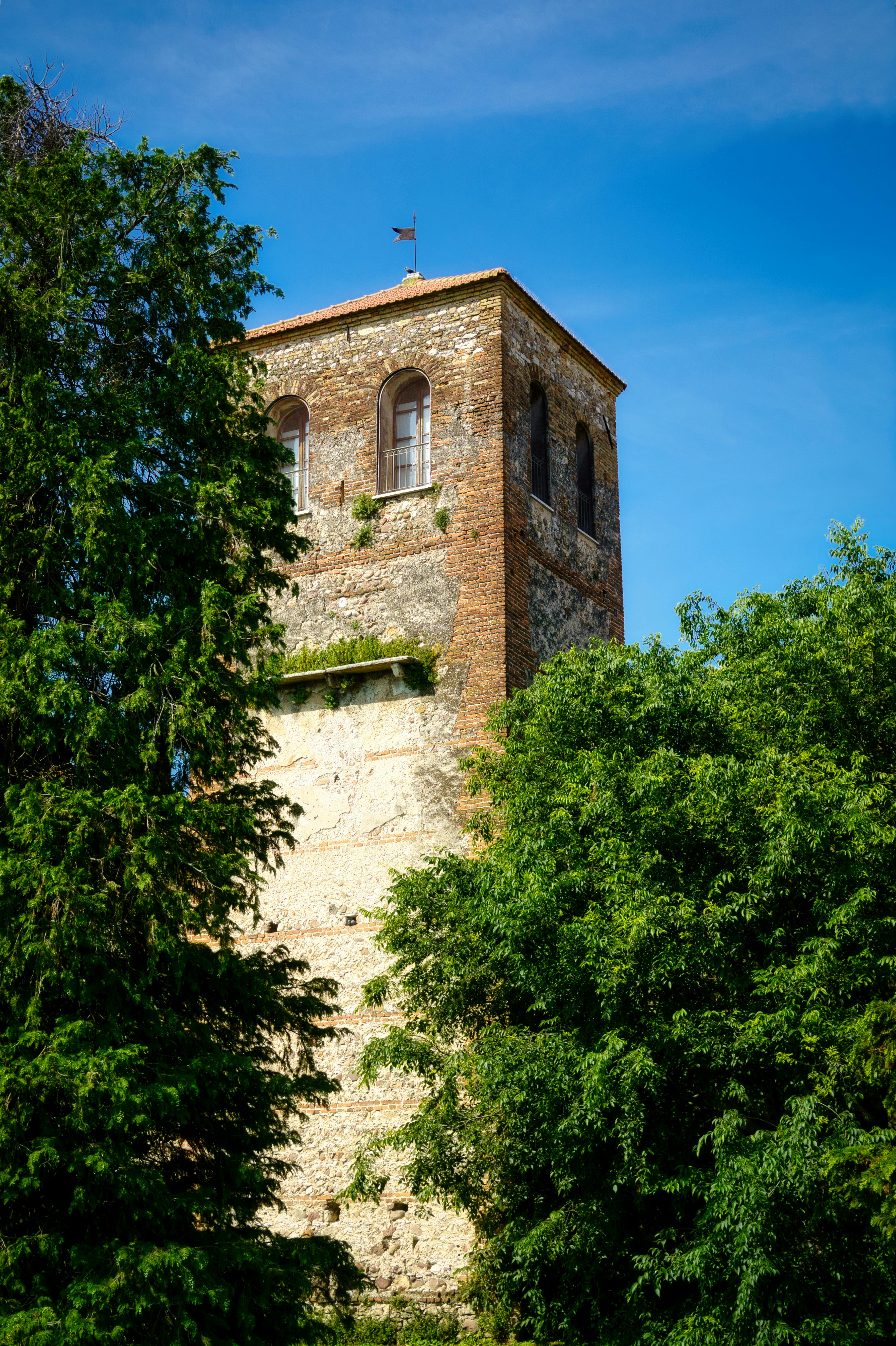 Stone tower nestled among lush green trees under a bright blue sky in Veneto, Italy.
