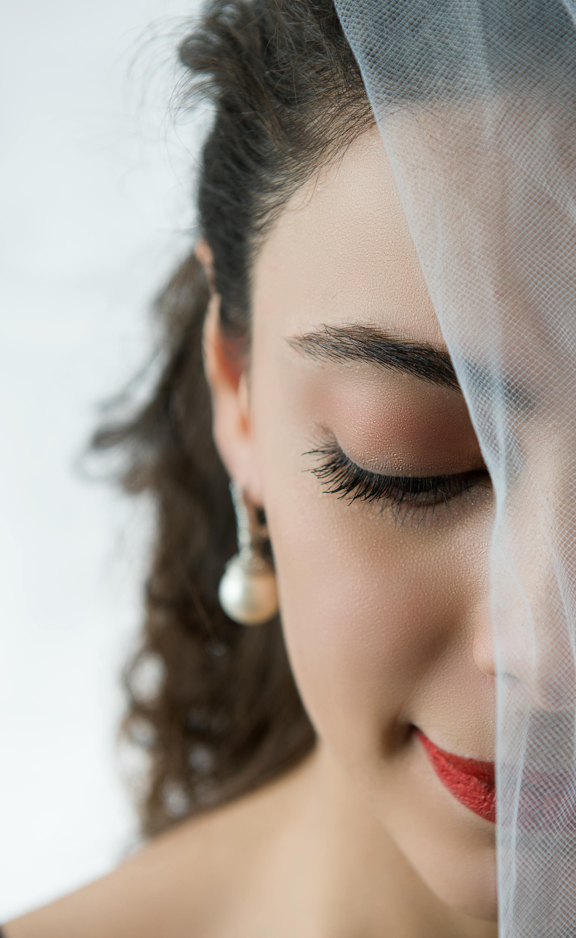 Close-up of a young woman wearing a veil and pearl earring, representing elegance and fashion.