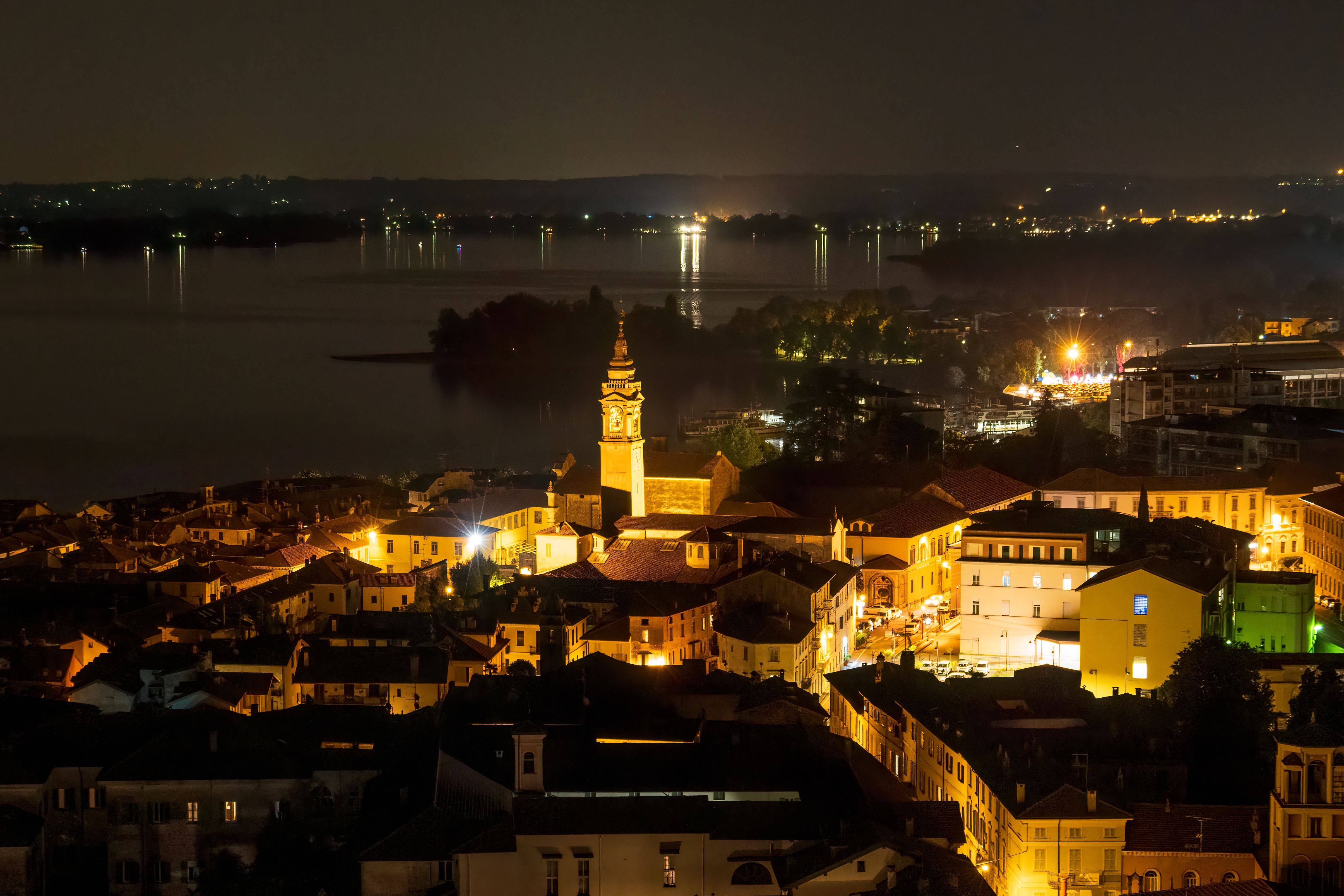 A captivating night panorama featuring Angera town illuminated beside a tranquil lake.