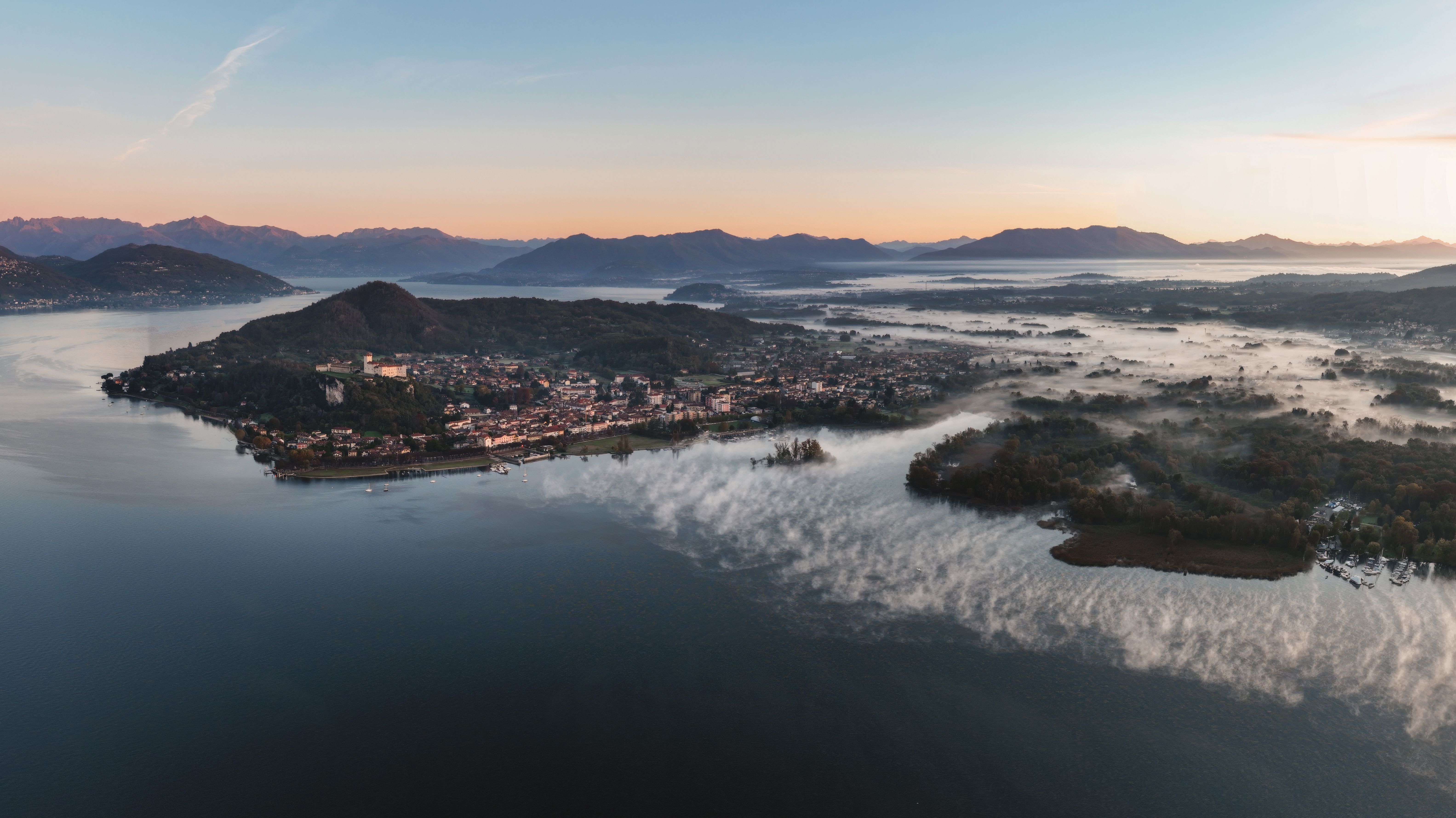 Stunning aerial view of Lake Maggiore with misty morning fog and surrounding hills at sunrise.