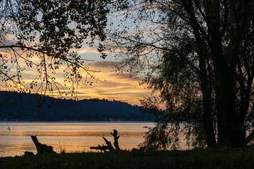 Free Peaceful lake view with silhouetted trees against a vibrant sunset sky. Stock Photo