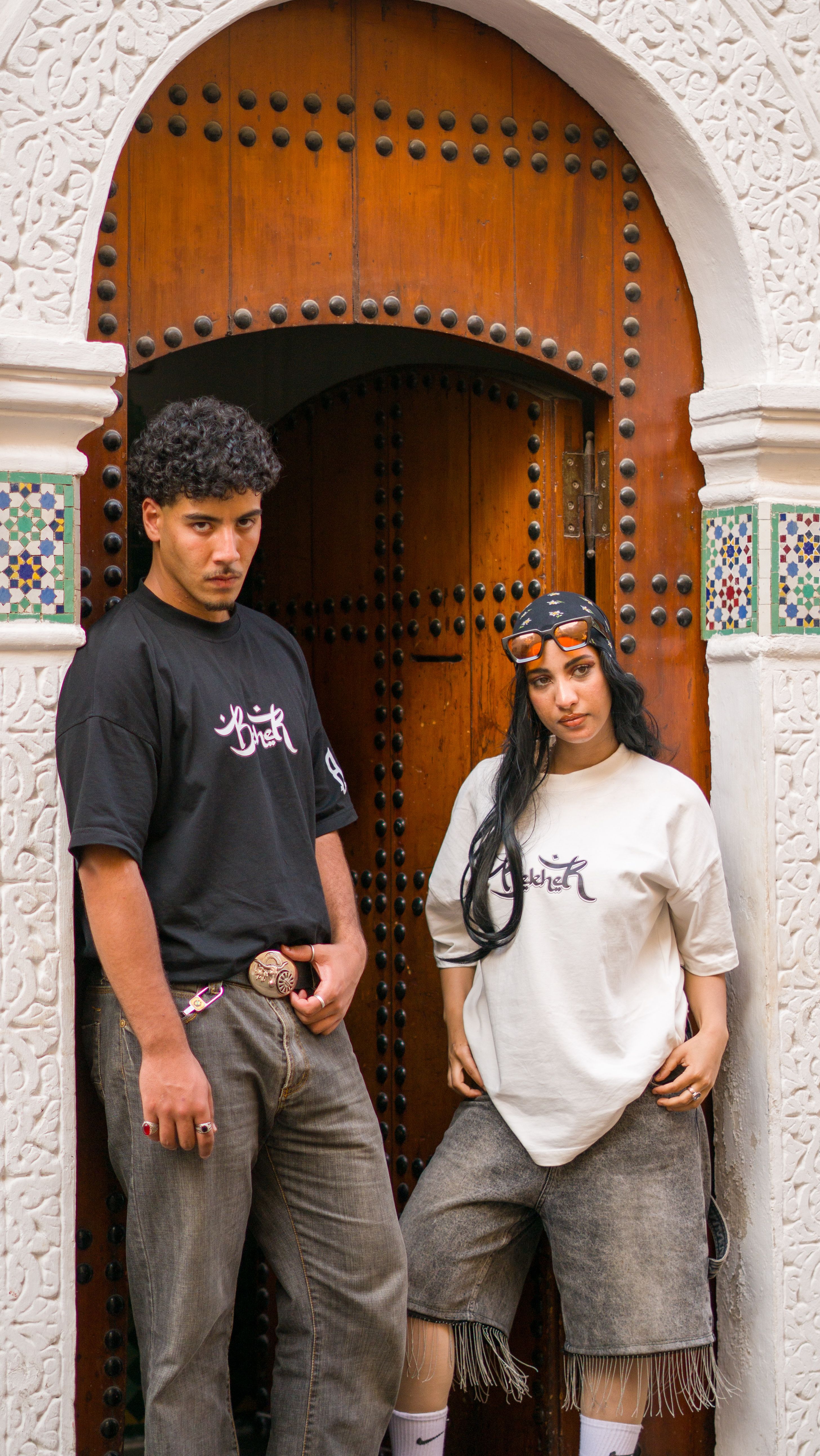 Stylish young adults posing by a traditional Moroccan doorway in vibrant streetwear fashion.