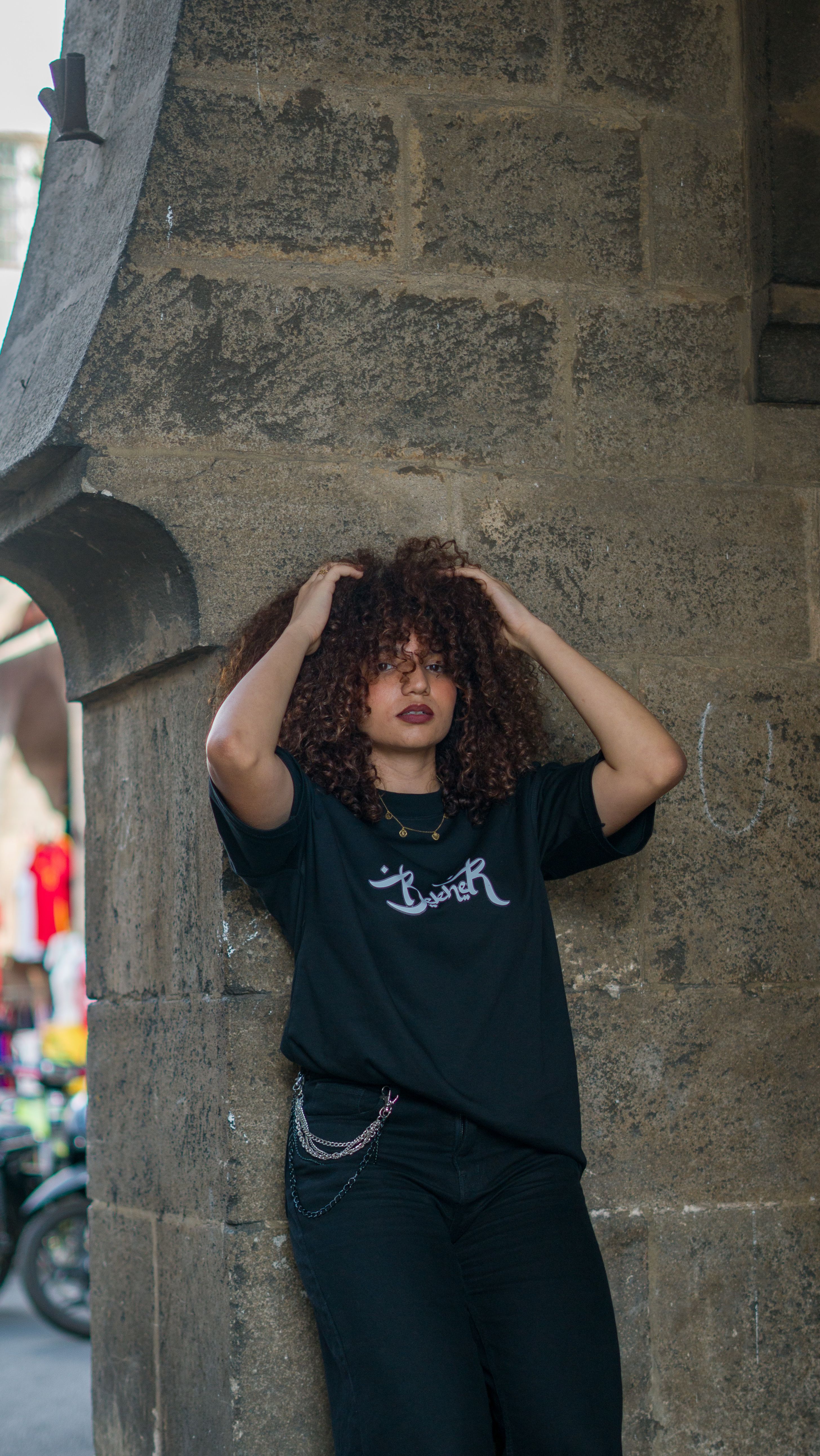 Stylish woman poses against a stone wall in a bustling Moroccan street scene.