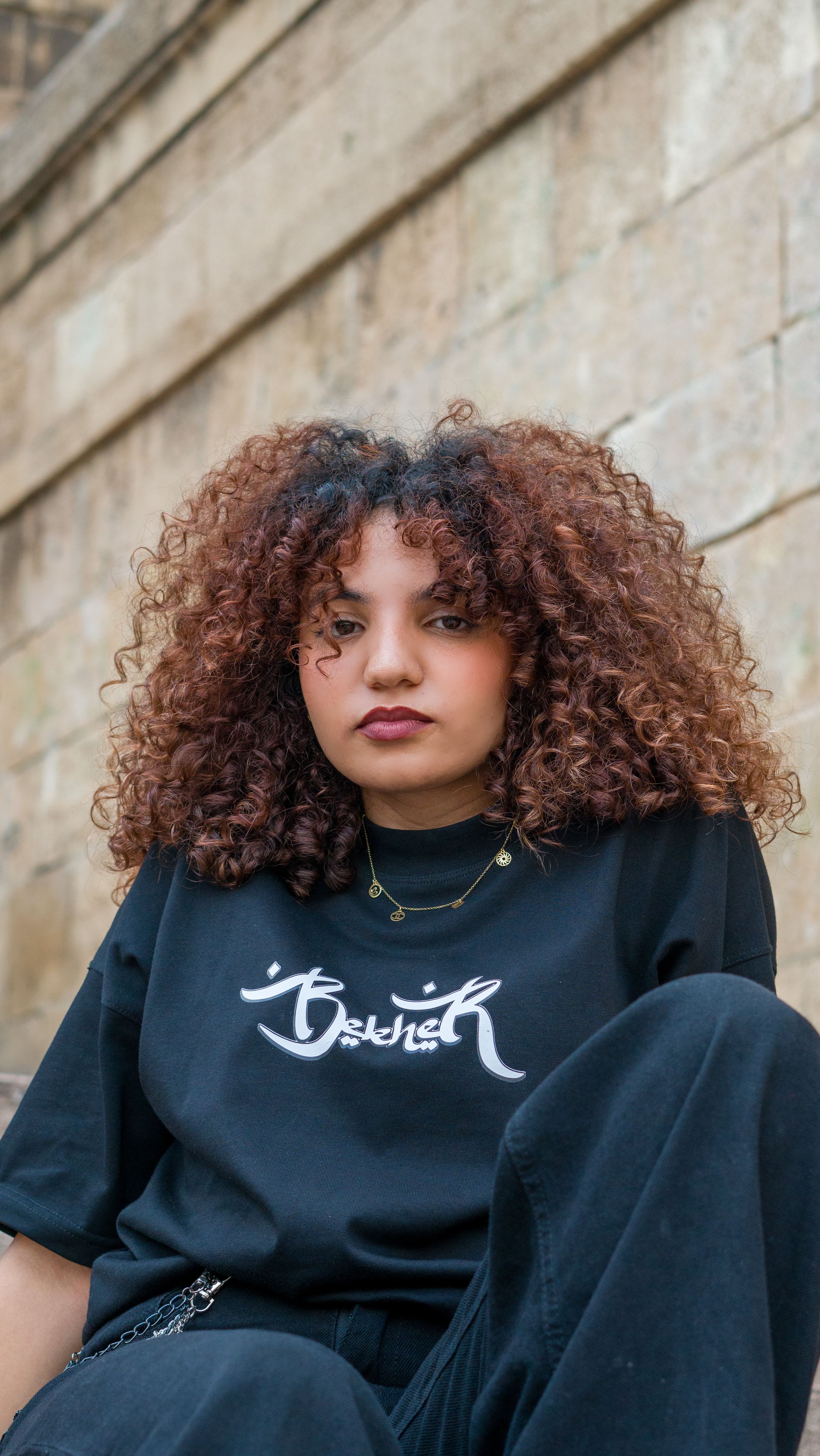 Confident young woman with curly hair wearing street fashion attire in an urban setting.