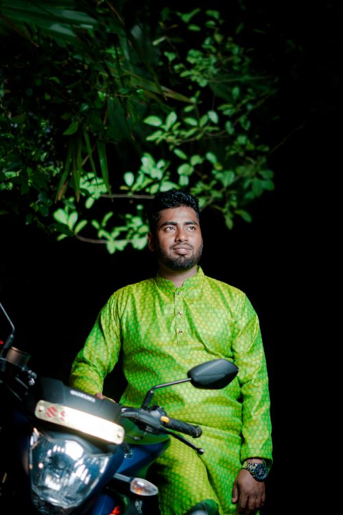 Free A man in vibrant traditional dress sits on a motorcycle, surrounded by greenery at night. Stock Photo