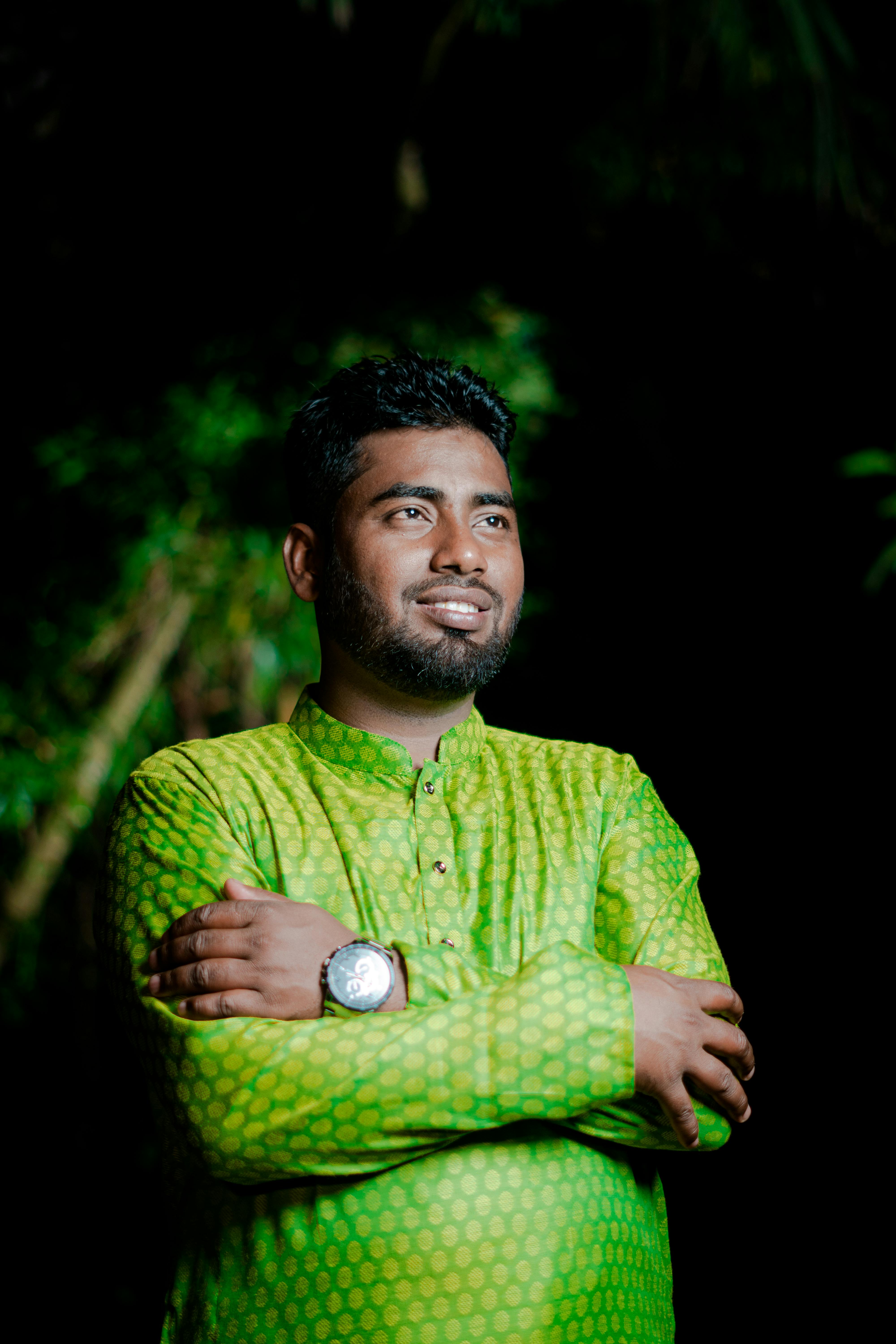 Confident man in traditional green outfit posing outdoors at night, expressing joy.